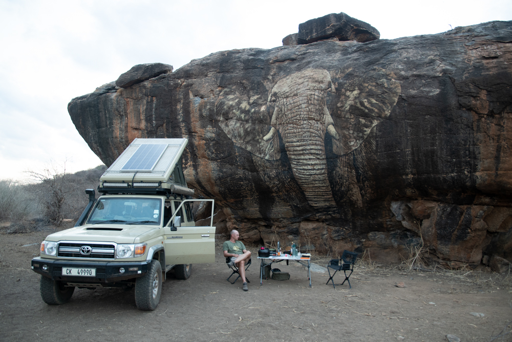 A campsite set up in front of a large rock with an elephant painted on it
